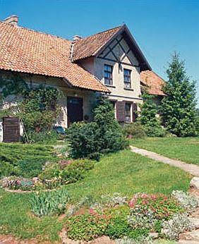 Rozłożysty parterowy dom z dwuspadowym dachem krytym czerwoną ceramiczną dachówką doskonale kontrastuje z bujną zielenią. 